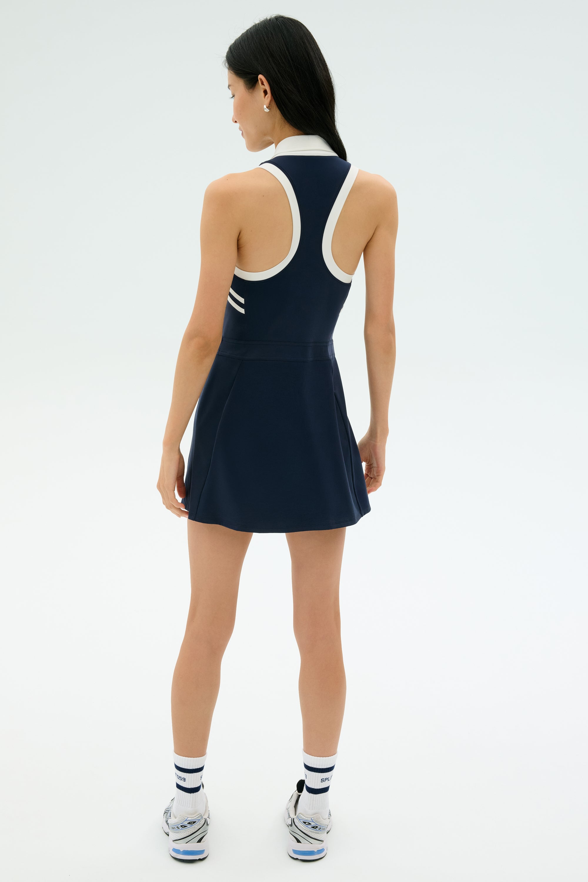 A woman faces away, wearing the SPLITS59 Austin Rigor Dress in Indigo/White, paired with striped white socks and athletic shoes against a plain light background.
