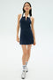 A woman wears the SPLITS59 Austin Rigor Dress in Indigo/White, paired with white socks featuring navy stripes and white sneakers, standing against a plain light background.
