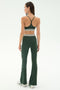 A woman stands facing away in the SPLITS59 Cali Active Rib Bra - Heather Military, paired with matching flared leggings featuring white stripes and white sneakers, set against a plain light background.