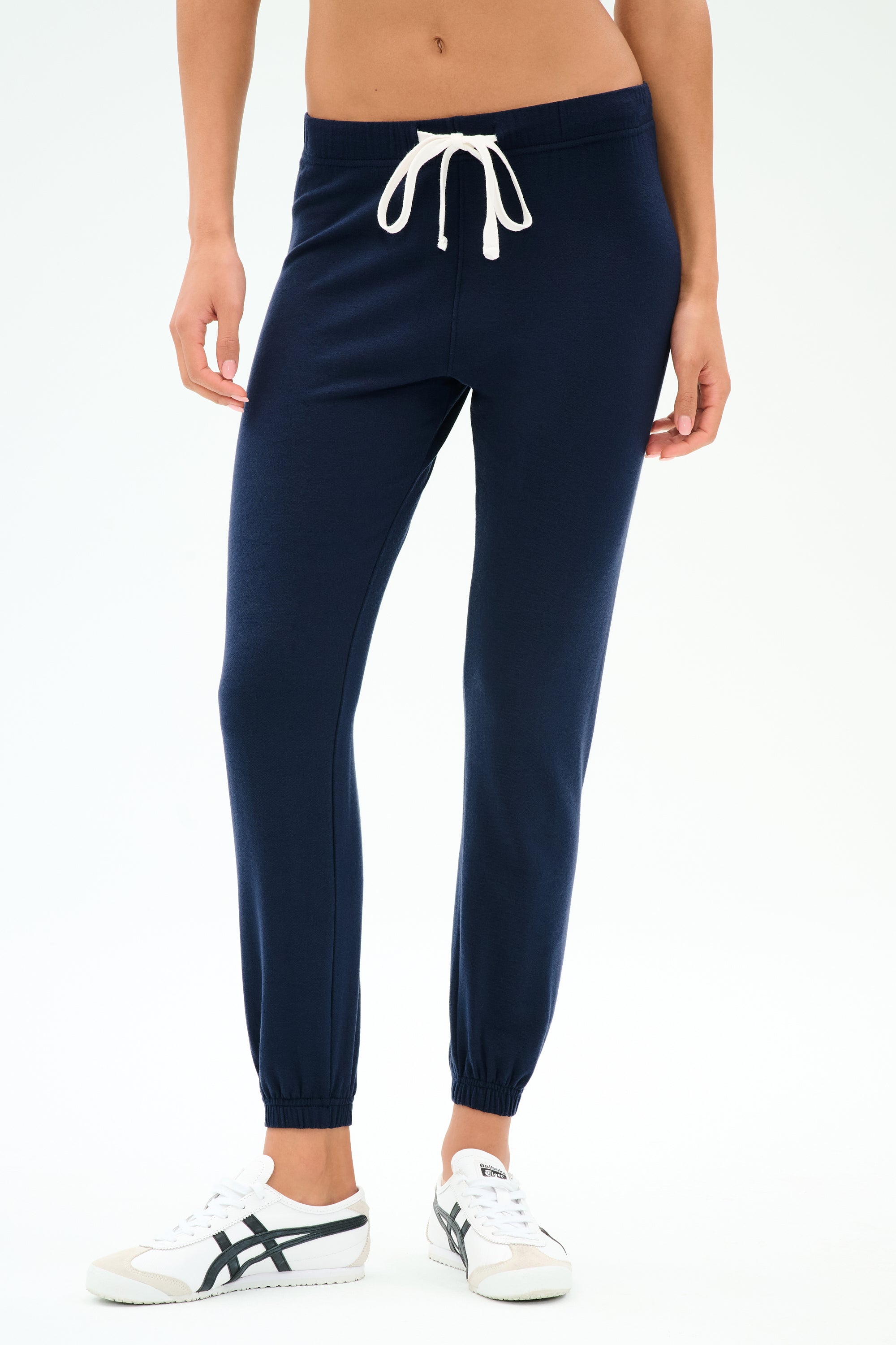 Model wears the SPLITS59 Sonja Fleece Sweatpant in Indigo—navy blue, slouchy-soft joggers with a white drawstring and white sneakers, crafted from ultra luxe fleece in Los Angeles—against a plain background.