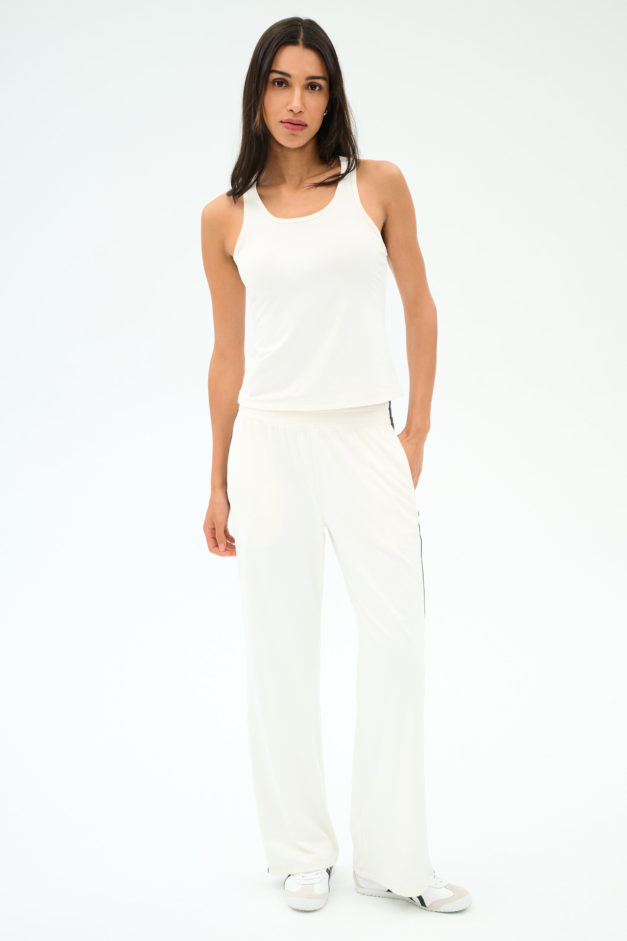 A woman stands against a plain white background wearing the SPLITS59 Mel Airweight Lite Tank in white, paired with white wide-leg pants and white sneakers.