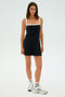 A person models the SPLITS59 Monah Rigor Dress in Black/White, made from a soft fabric blend with white straps. They pair it with silver sneakers and white socks against a light blue background for a serene touch.