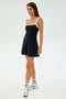 A person wearing the Monah Rigor Dress by SPLITS59 in black and white stands against a gray background, paired with white socks and silver sneakers.