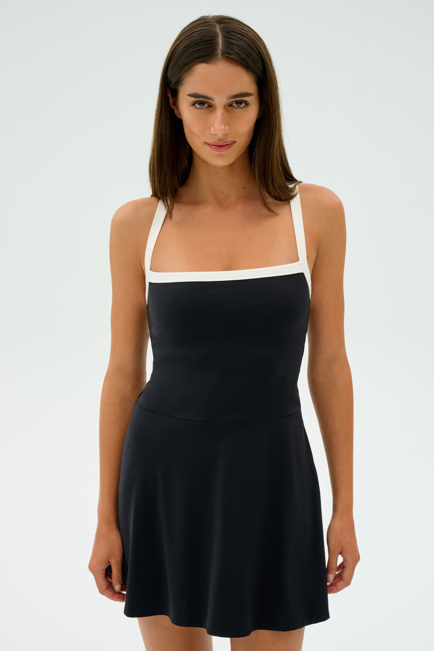 A person with long dark hair wears the Monah Rigor Dress by SPLITS59, featuring white straps and a square neckline, standing against a plain white background.