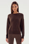 A woman with long straight hair stands facing the camera, wearing a plain dark long-sleeve top and matching leggings against a neutral background, showcasing the Sonja Fleece Sweatshirt in Dark Chocolate by SPLITS59.