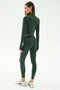 Woman standing and facing away, wearing SPLITS59’s Bailey Active Rib High Waist 7/8 leggings and matching dark green top in Heather Military, paired with white sneakers—ideal activewear for workouts.