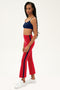 A woman stands in profile wearing the SPLITS59 Raquel High Waist Crop in Pirate Red/Indigo with white sneakers, set against a plain background.