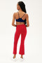 A woman faces away from the camera, wearing a navy sports bra and SPLITS59 Raquel High Waist Crop pants in Pirate Red/Indigo, crafted from 4-way stretch fabric, styled with white sneakers against a plain background.