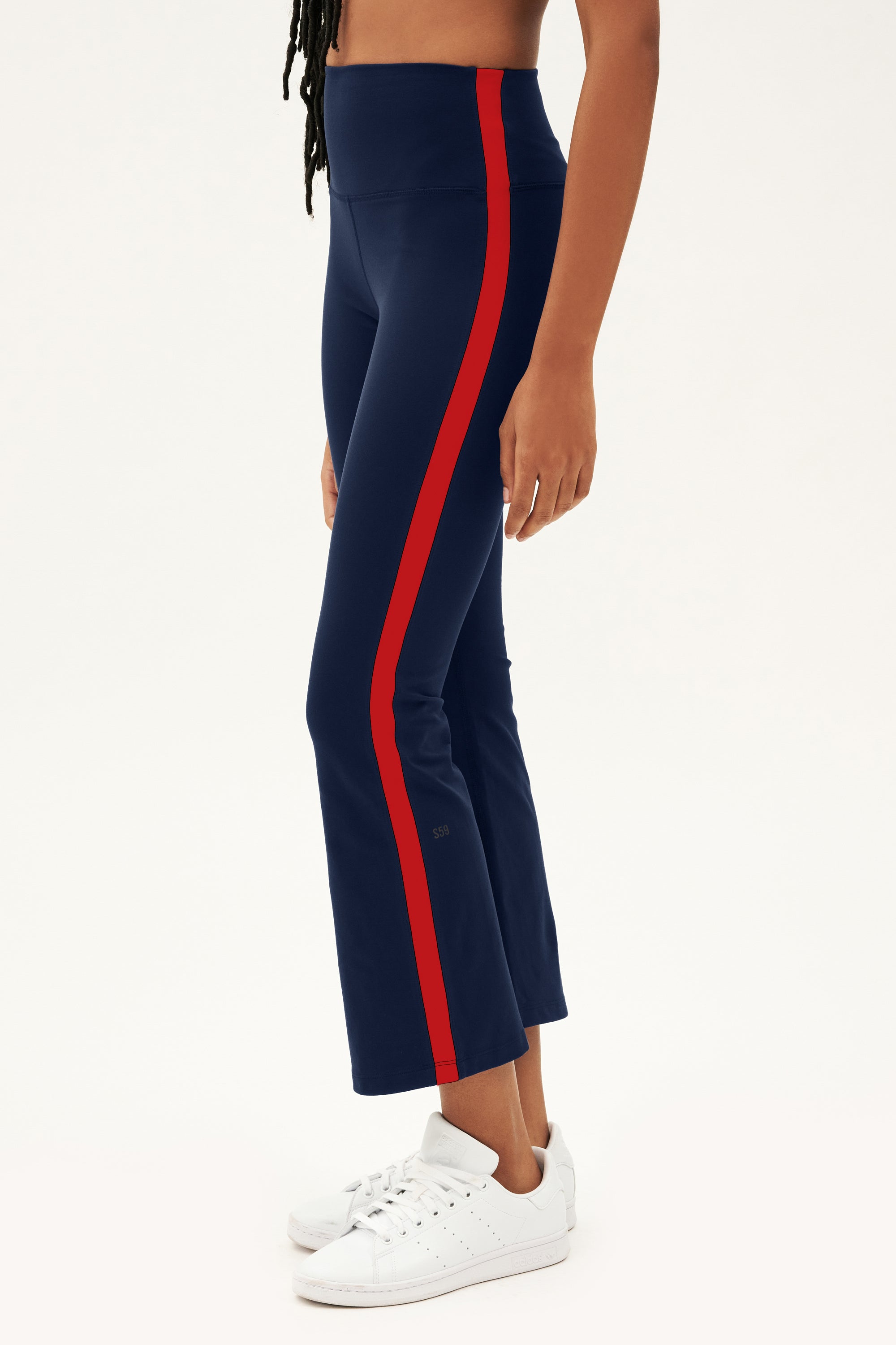 A person wears the SPLITS59 Raquel High Waist Supplex Crop in Indigo/Pirate Red, featuring a red side stripe and 4-way stretch fabric, paired with white sneakers against a white background—ideal for gym or casual wear.