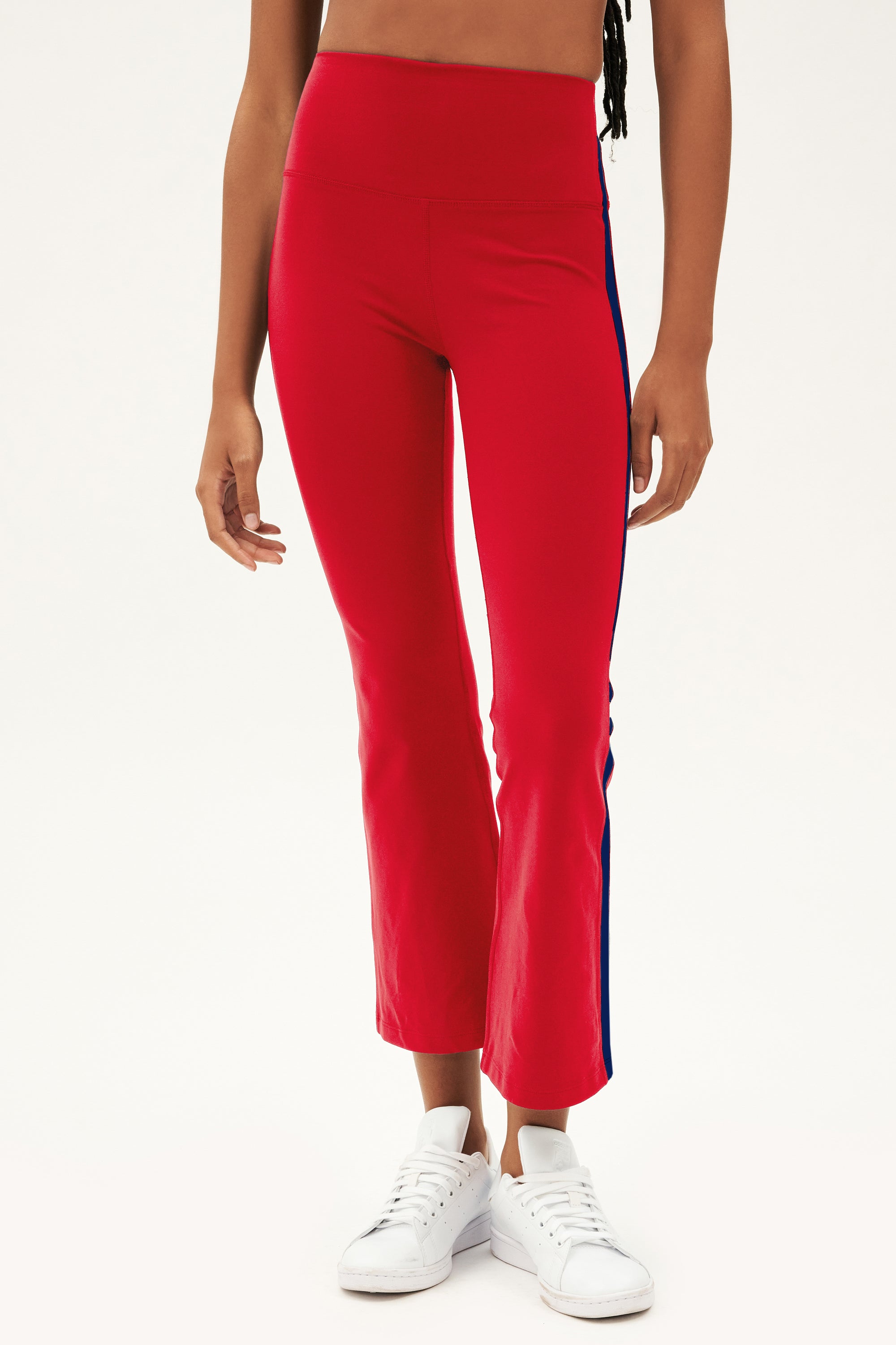 Raquel wears SPLITS59 Raquel High Waist Supplex Crop pants in Pirate Red/Indigo with white sneakers, standing against a plain background.
