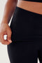 Close-up of a person wearing Raquel Airweight Foldover Flare - Black by SPLITS59, with the left hand tugging at the waistband, revealing the spandex fabric's stretch.