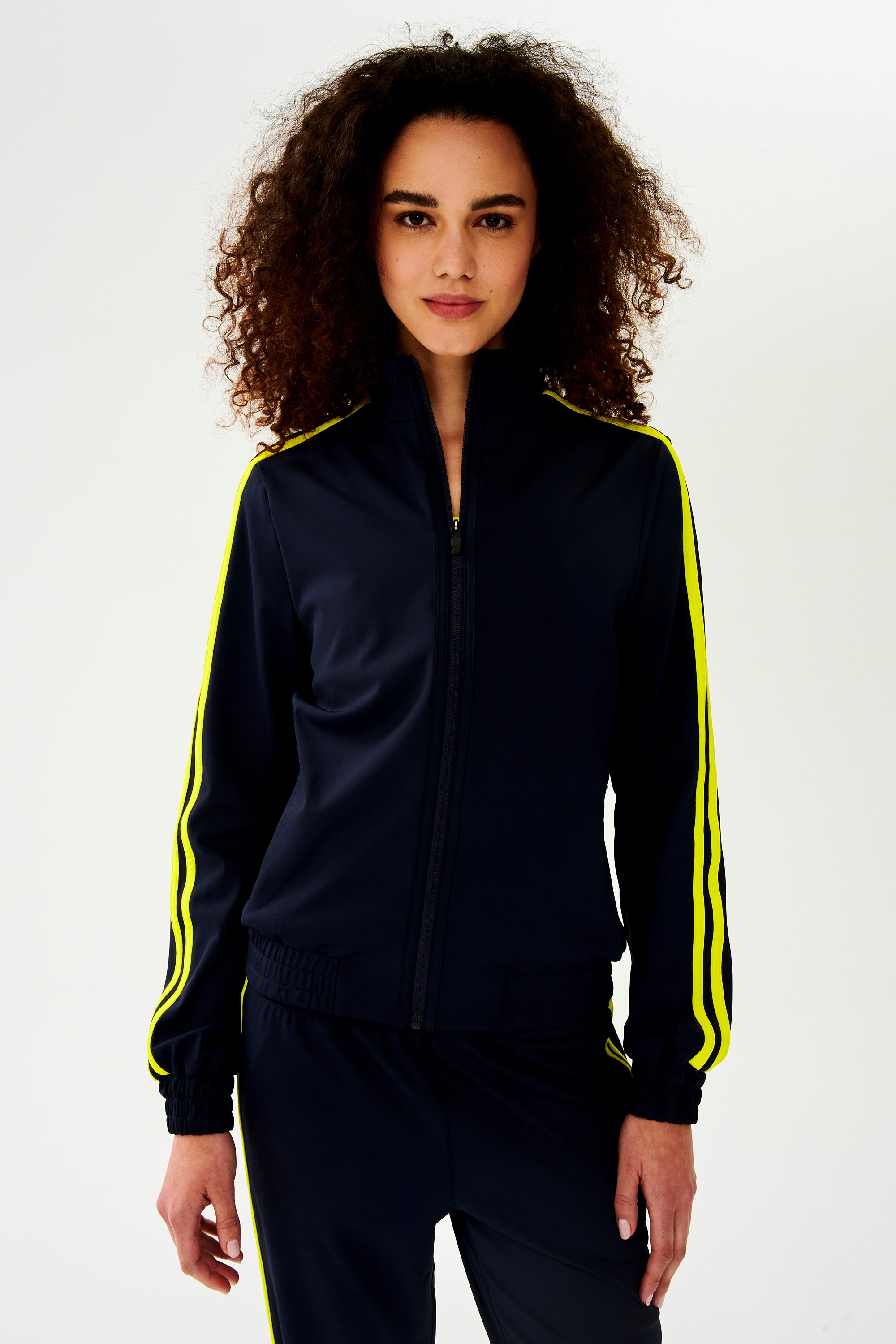 A woman warming up in a luxurious SPLITS59 Fox Techflex Jacket - Indigo/Chartreuse.