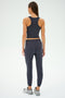 A person wearing the SPLITS59 Sonja Fleece Sweatpant in Graphite and a sleeveless top, paired with sneakers, stands against a plain background, facing away.