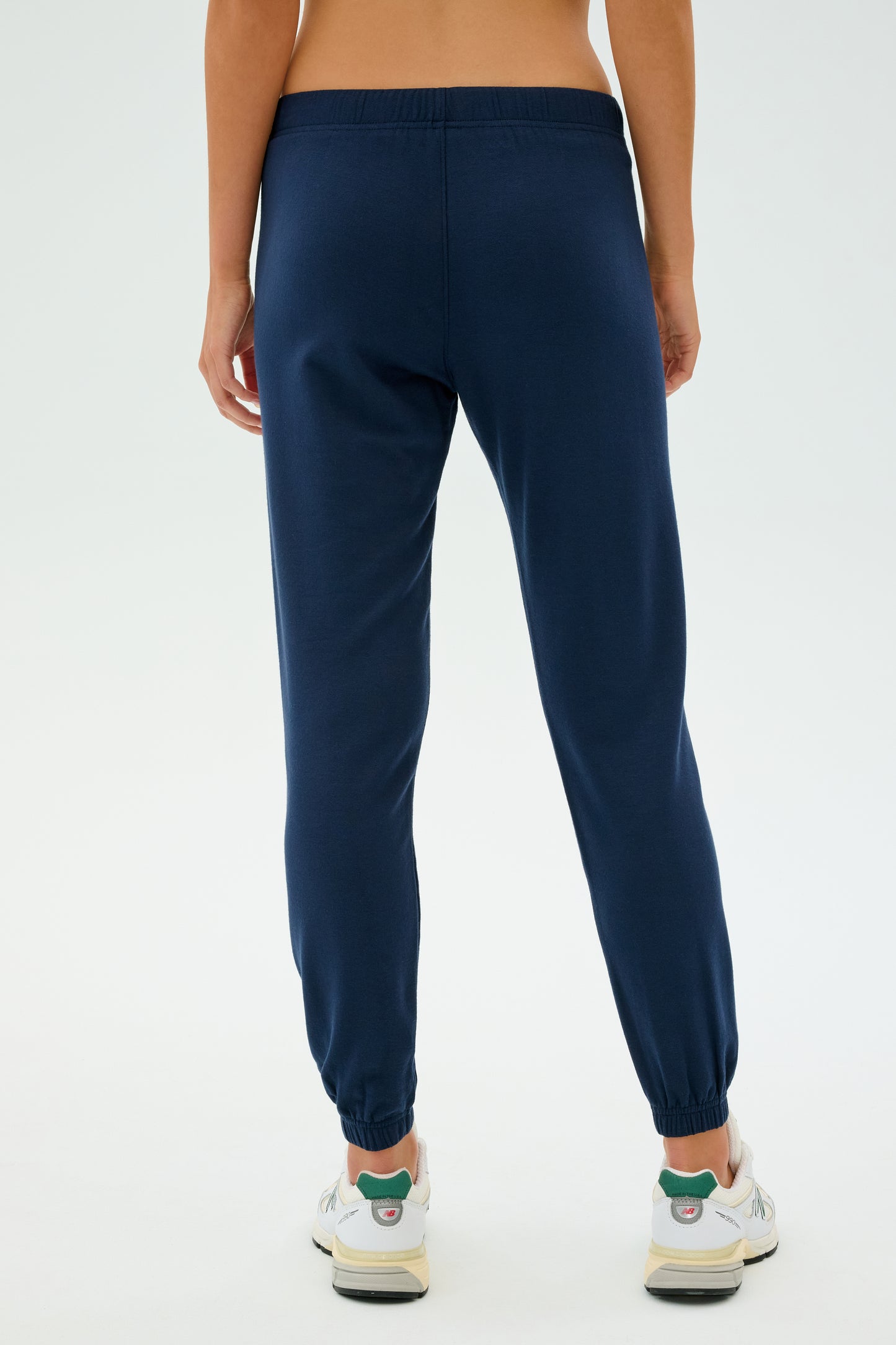 Rear view of a person wearing SPLITS59's Sonja Fleece Sweatpant in Indigo paired with white sneakers against a plain background, ready for workouts.