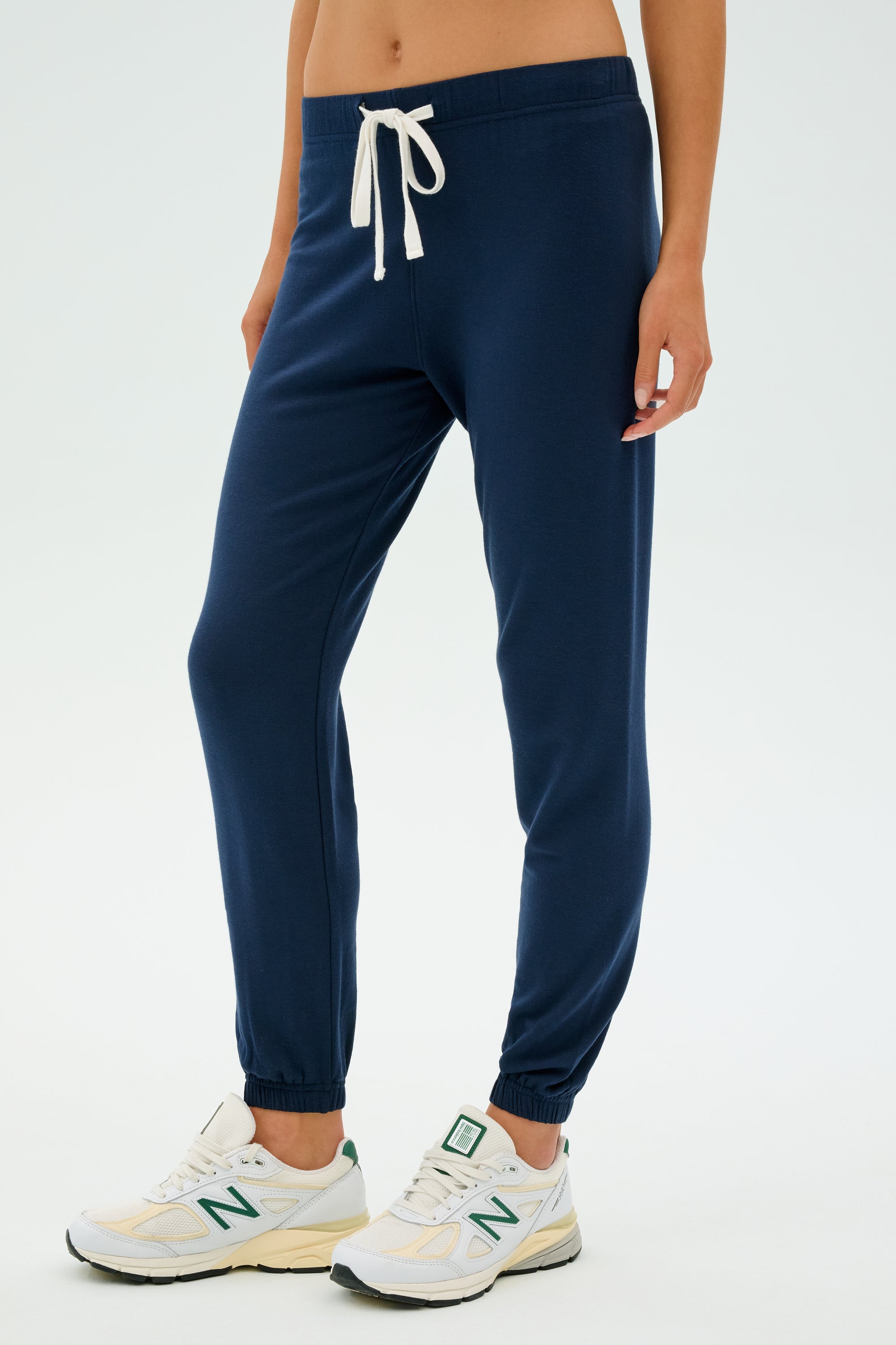 Someone wearing SPLITS59's Sonja Fleece Sweatpant in Indigo and white sneakers stands against a light background, perfect for cool weather workouts.