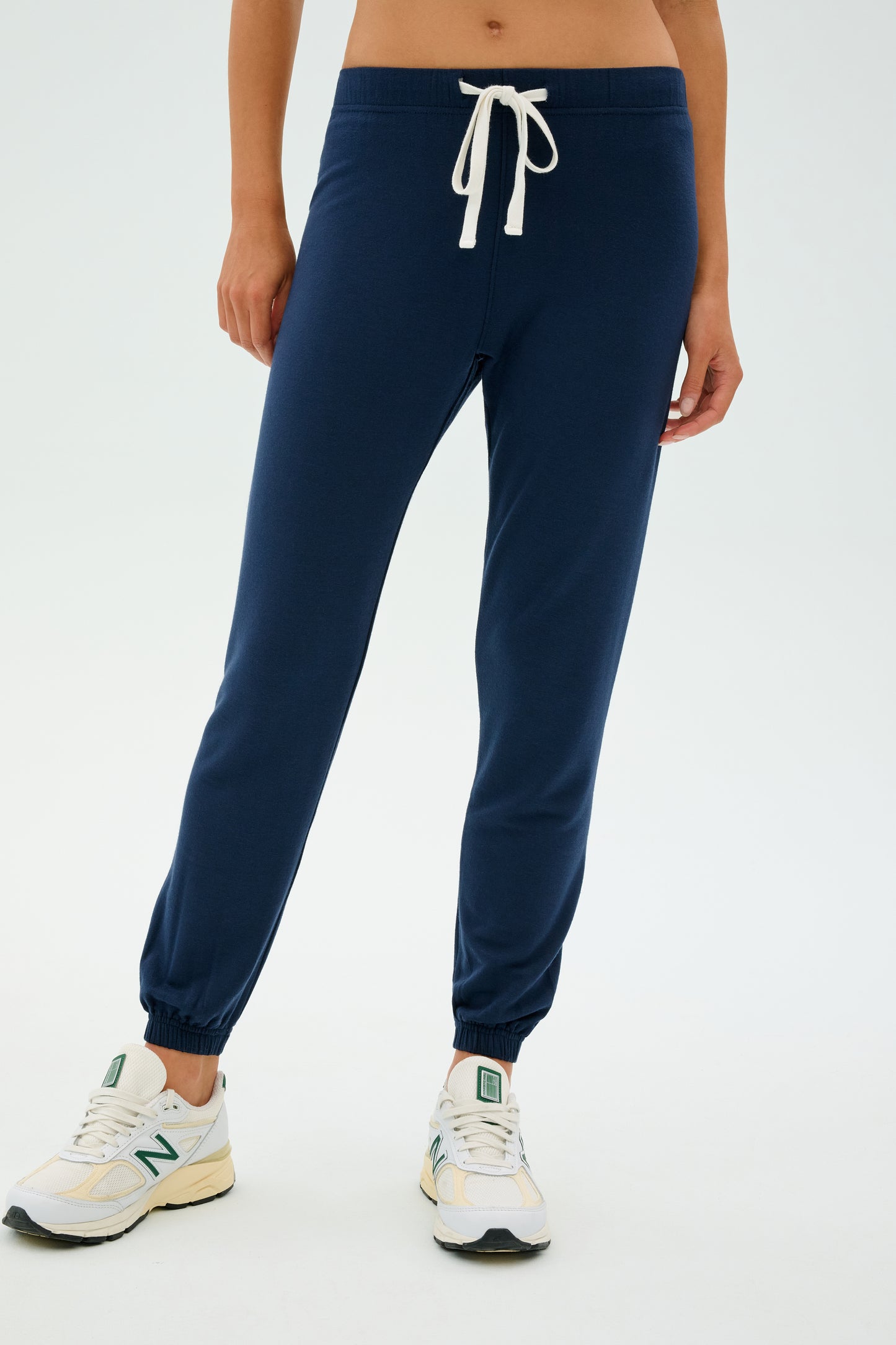 Someone wearing Sonja Fleece Sweatpant - Indigo by SPLITS59, paired with white sneakers featuring green accents and a white drawstring. Ideal for cool weather workouts.