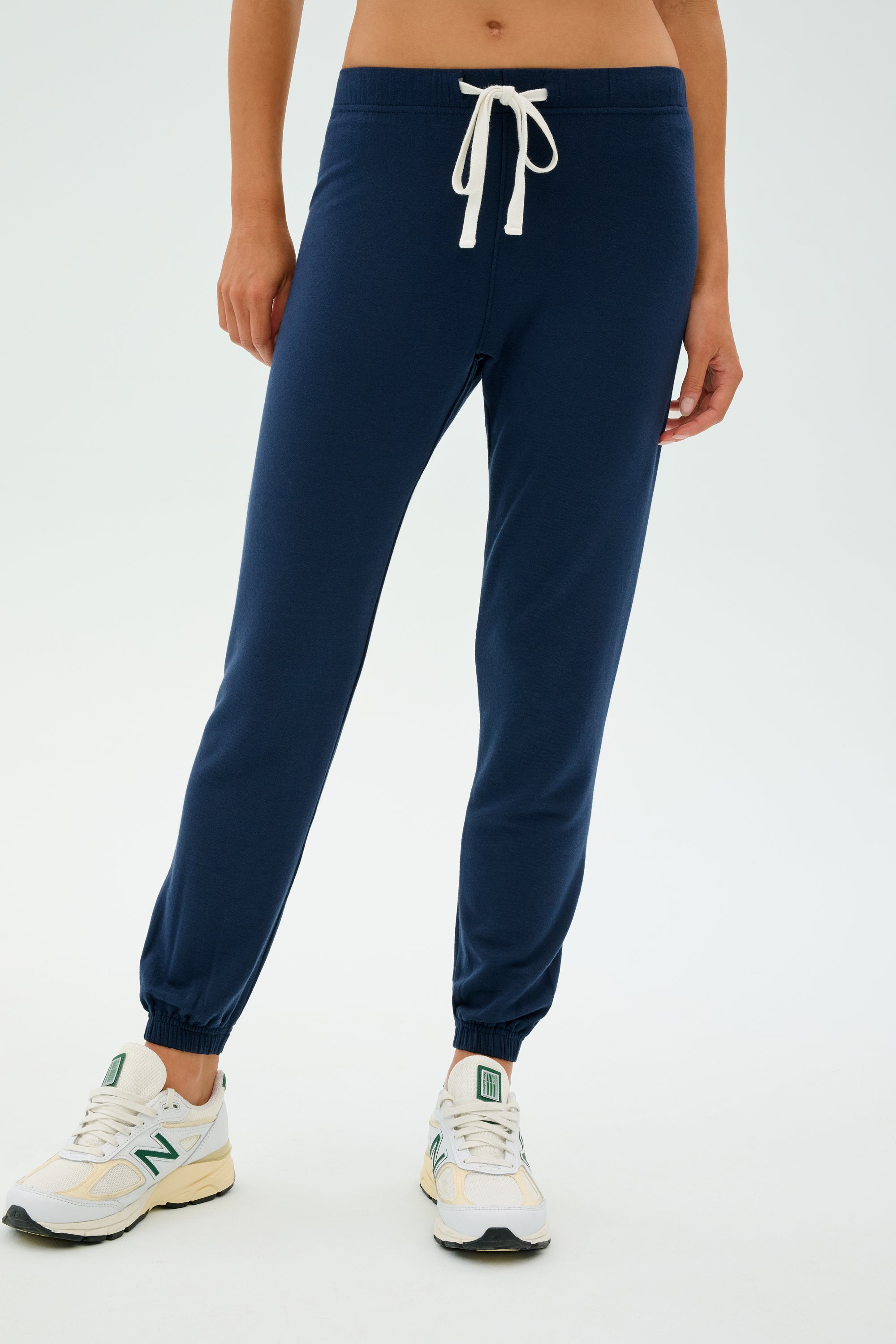 Someone wearing Sonja Fleece Sweatpant - Indigo by SPLITS59, paired with white sneakers featuring green accents and a white drawstring. Ideal for cool weather workouts.