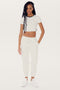 A person with long braided hair, wearing a SPLITS59 Airweight S/S Crop - White/Black and white jogger pants made of spandex, along with matching white sneakers, stands facing the camera with one hand in their pocket.