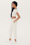 A woman with long braided hair wears an Airweight S/S Crop - White/Black by SPLITS59, white jogger pants made of spandex, and white sneakers, standing in profile against a plain white background.