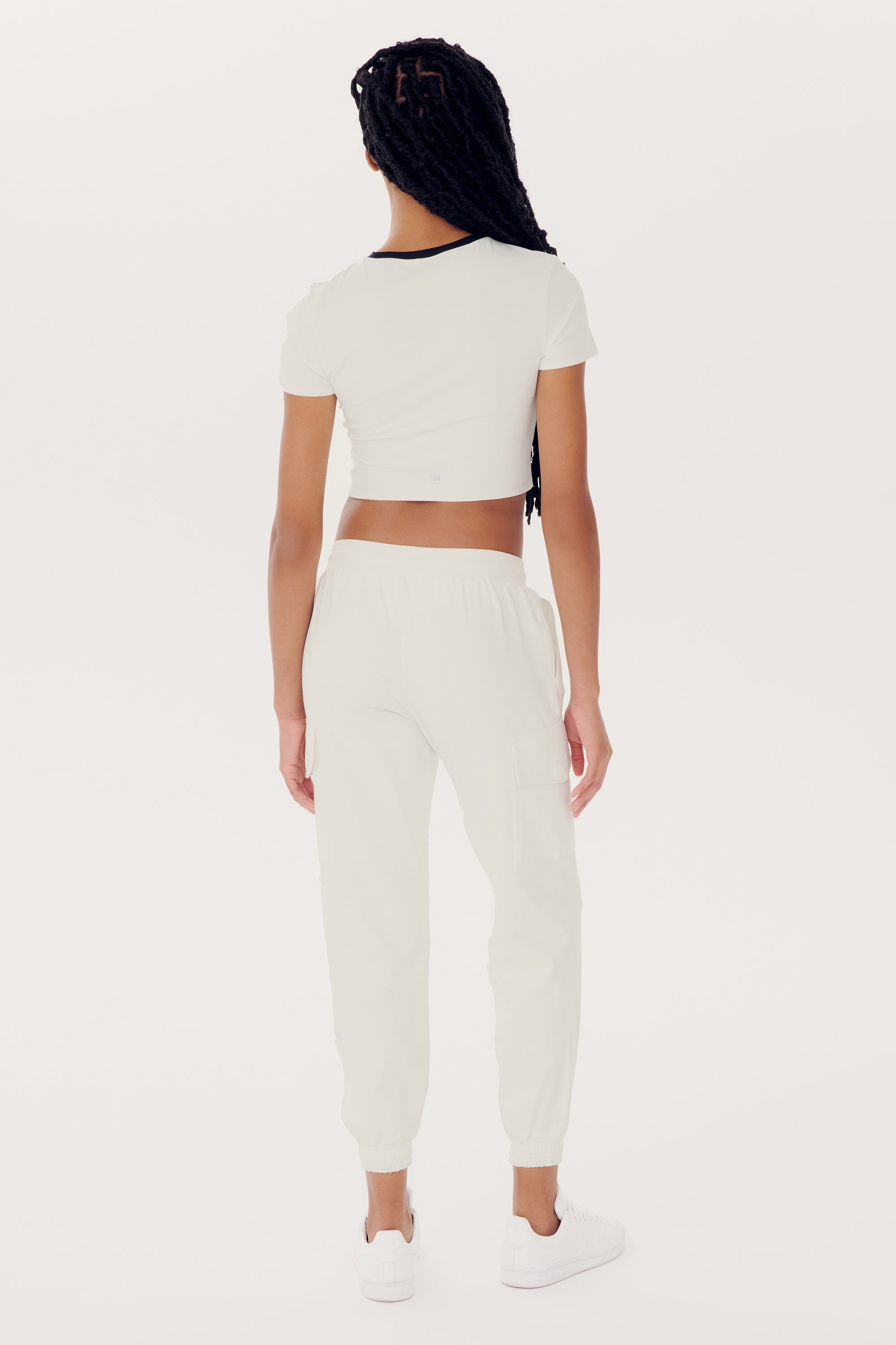 Person standing with their back to the camera, wearing an Airweight S/S Crop - White/Black by SPLITS59, matching joggers, and white sneakers.