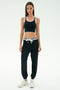 A woman faces forward in a black sports bra and SPLITS59 Andie Oversized Fleece Sweatpant W/ Stripe, paired with white sneakers, set against a plain light background.