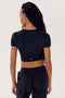 Person with long braided hair wearing a SPLITS59 Airweight S/S Crop - Black and dark pants, viewed from the back against a plain white background.
