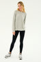A woman stands in a neutral pose wearing an Andie Fleece Sweatshirt in Heather Grey from SPLITS59, paired with black leggings and grey sneakers, against a plain white background.