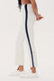 A person wearing white high waist SPLITS59 Raquel High Waist Crop - White/Indigo pants made from 4-way stretch supplex fabric with a dark stripe running down the side, paired with white sneakers. They are standing in a side profile with hands clasped behind their back.