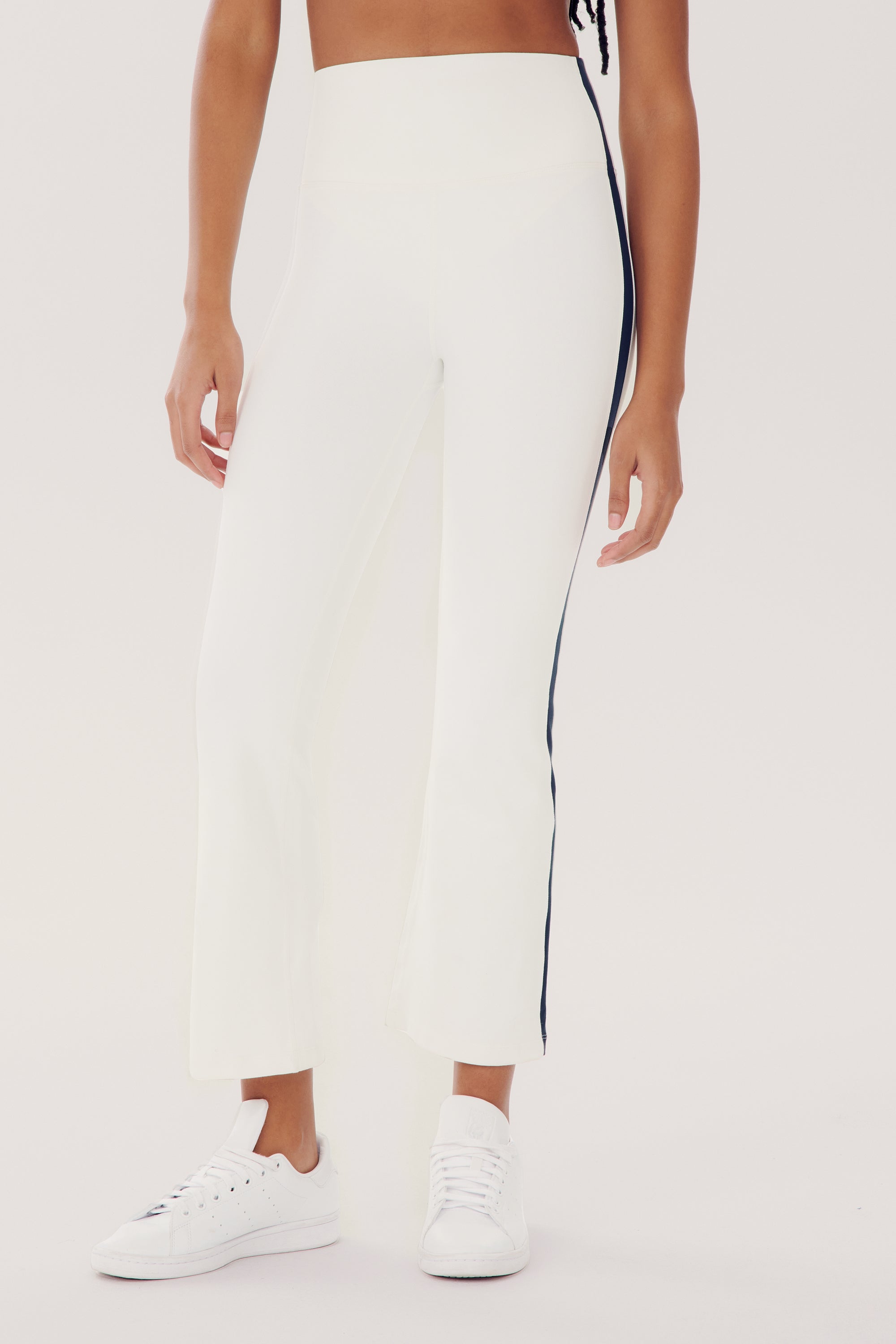 Person wearing high-waisted Raquel High Waist Crop - White/Indigo by SPLITS59 with a black stripe down the side, crafted from 4-way stretch supplex fabric, paired with white sneakers.