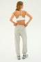 A person in a white sports bra is standing and adjusting the waistband of their Andie Oversized Fleece Sweatpant in Heather Grey by SPLITS59. The person is facing away from the camera with their head turned slightly to the side, making it perfect for cool-weather workouts.