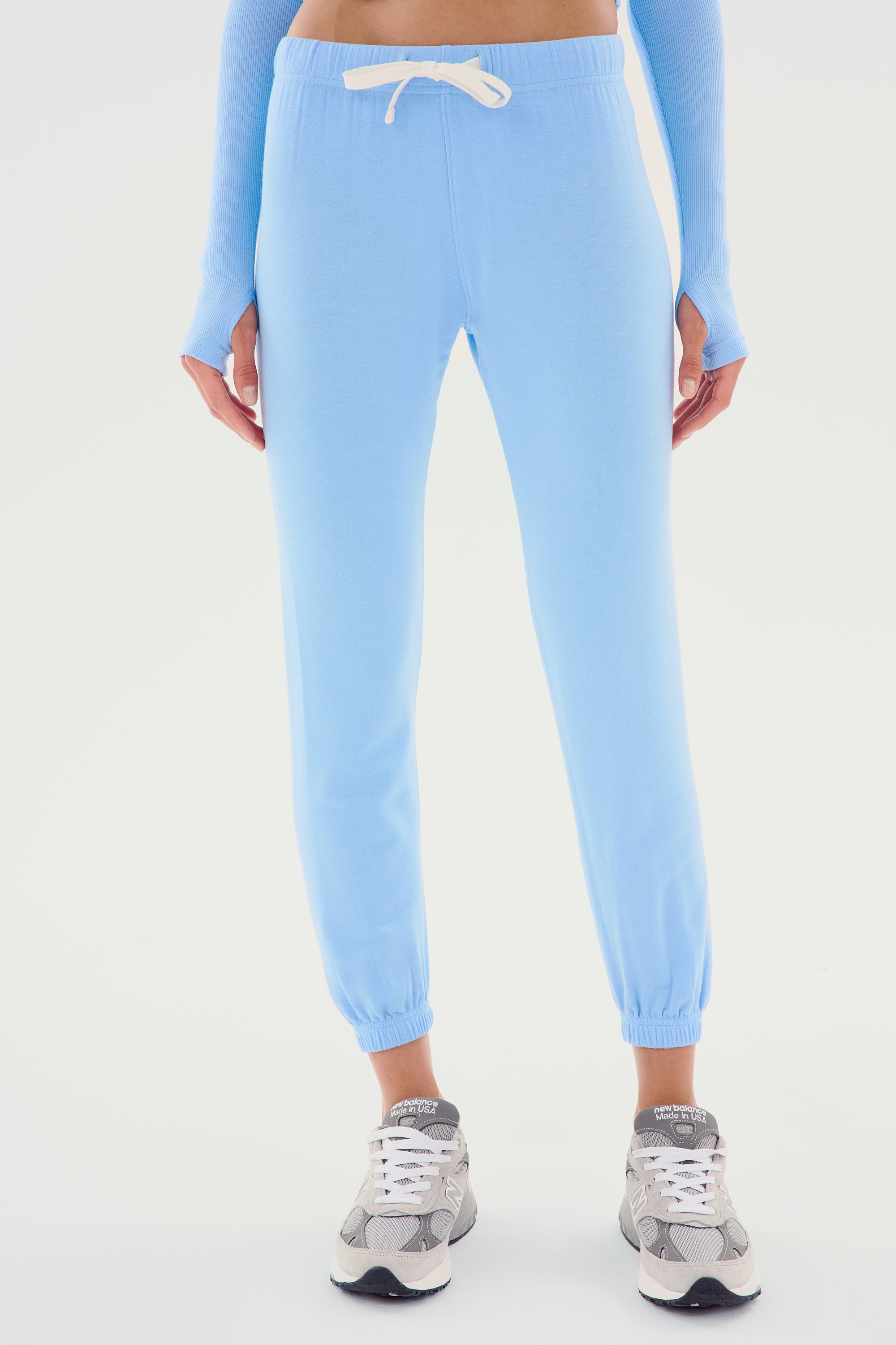 A person wearing the Sonja Fleece Sweatpant - Skylight by SPLITS59, featuring slouchy-soft, light blue fabric with white drawstrings, paired with gray sneakers—perfect for cool weather workouts.