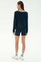 A woman faces away, wearing the SPLITS59 Sonja Fleece Sweatshirt w/ Stripe in indigo, navy shorts, white crew socks with stripes, and white sneakers against a white background.