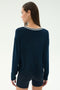A woman with straight brown hair faces away, wearing the SPLITS59 Sonja Fleece Sweatshirt W/ Stripe in indigo and matching shorts, set against a plain light background.