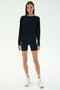 A woman faces forward on a plain light background wearing the SPLITS59 Sonja Fleece Sweatshirt W/ Stripe, black fitted shorts, white sneakers, and white socks with black stripes.