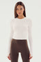 A person with long, straight hair wearing the SPLITS59 Louise Rib Long Sleeve Crop in white and high-waisted brown leggings, ready for yoga.