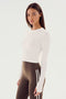 A woman stands against a plain background, wearing the SPLITS59 Louise Rib Long Sleeve Crop in white and brown leggings with white stripes, perfect for yoga or gym workouts.