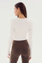 Revised Sentence: Rear view of a person with long hair, wearing the SPLITS59 Louise Rib Long Sleeve Crop in white and brown leggings with white side stripes, perfect for yoga.