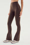 A person wearing SPLITS59's Raquel High Waist Flared Leggings in Dark Chocolate, made from 4-way stretch fabric, and white sneakers is standing against a plain background. Only the lower body is visible.