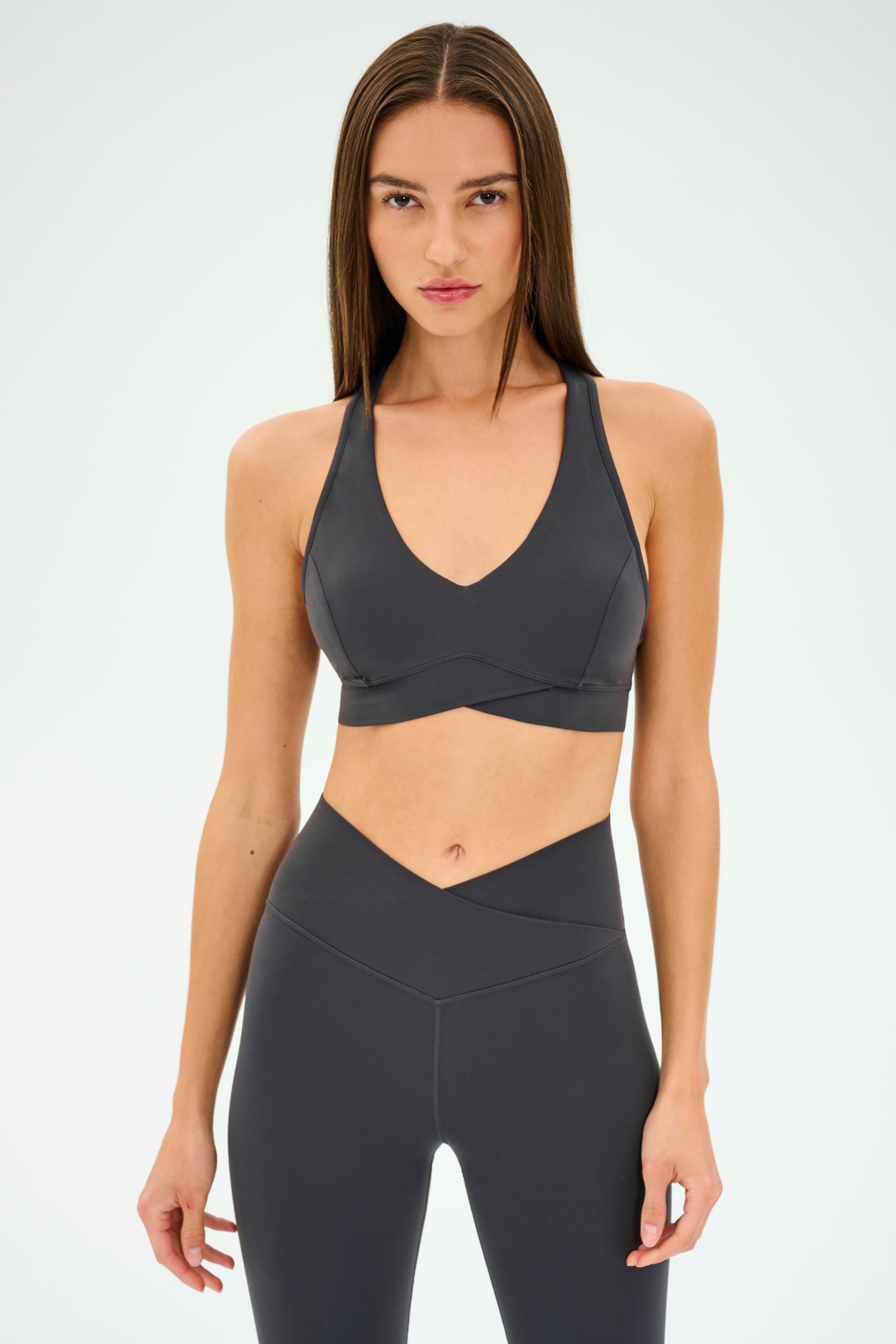 Wearing a SPLITS59 Mia Rigor Bra in Graphite and matching leggings, the person stands confidently against a plain white background, exuding a sense of multi-sport performance readiness.
