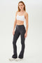 Full front side view of woman with straight blonde hair wearing dark gray high waist below ankle length legging with wide flared bottoms and white bra with spaghetti straps. Paired with white shoes.