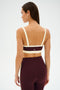 A woman faces away, wearing the SPLITS59 Monah Rigor Bra in Dark Cherry/Creme with matching high-waisted leggings featuring a side stripe.