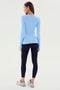 A person, turned away and standing, in the Skylight Louise Rib Long Sleeve top by SPLITS59, black leggings, and gray sneakers. Ready for some gym workouts or a yoga session.
