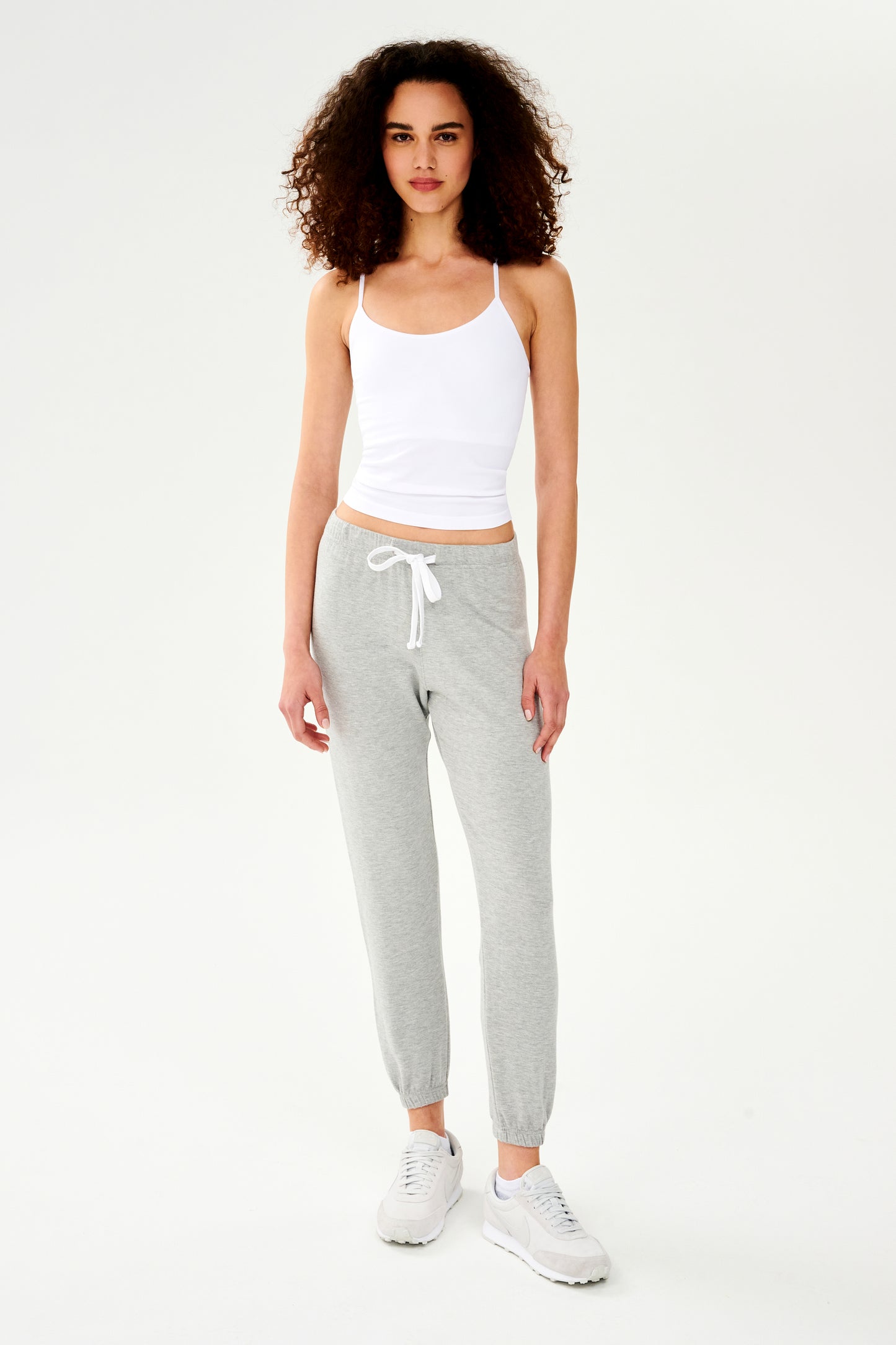 A woman wearing a SPLITS59 Loren Seamless Waist Length Tank in White with a shelf bra and grey sweatpants.