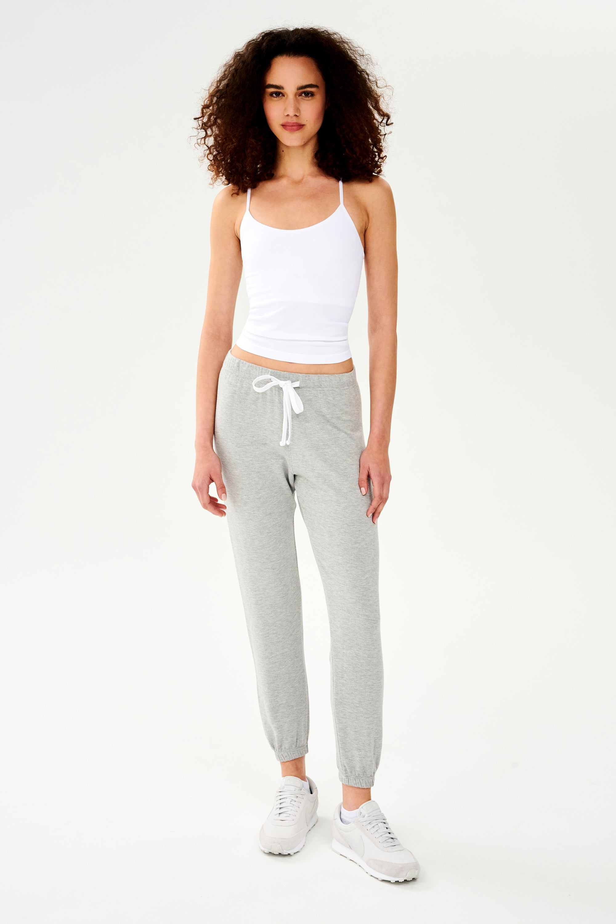 A woman wearing a SPLITS59 Loren Seamless Waist Length Tank in White with a shelf bra and grey sweatpants.