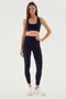 A woman wearing SPLITS59 Airweight High Waist Legging in black and white sneakers stands against a plain background. She faces forward with her right hand resting on her hip.