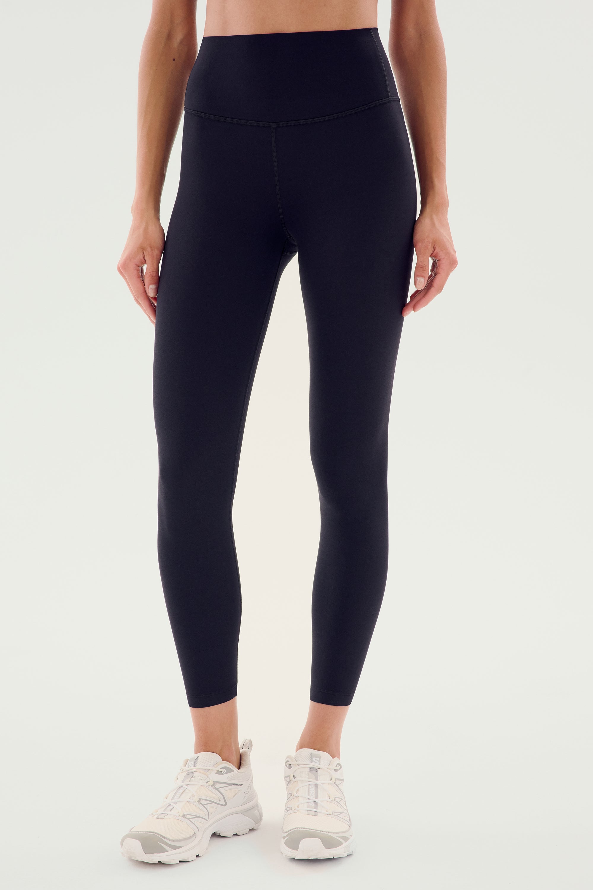 A person wearing the SPLITS59 Airweight High Waist Legging in black and white athletic shoes stands against a plain background, ready for hot yoga.
