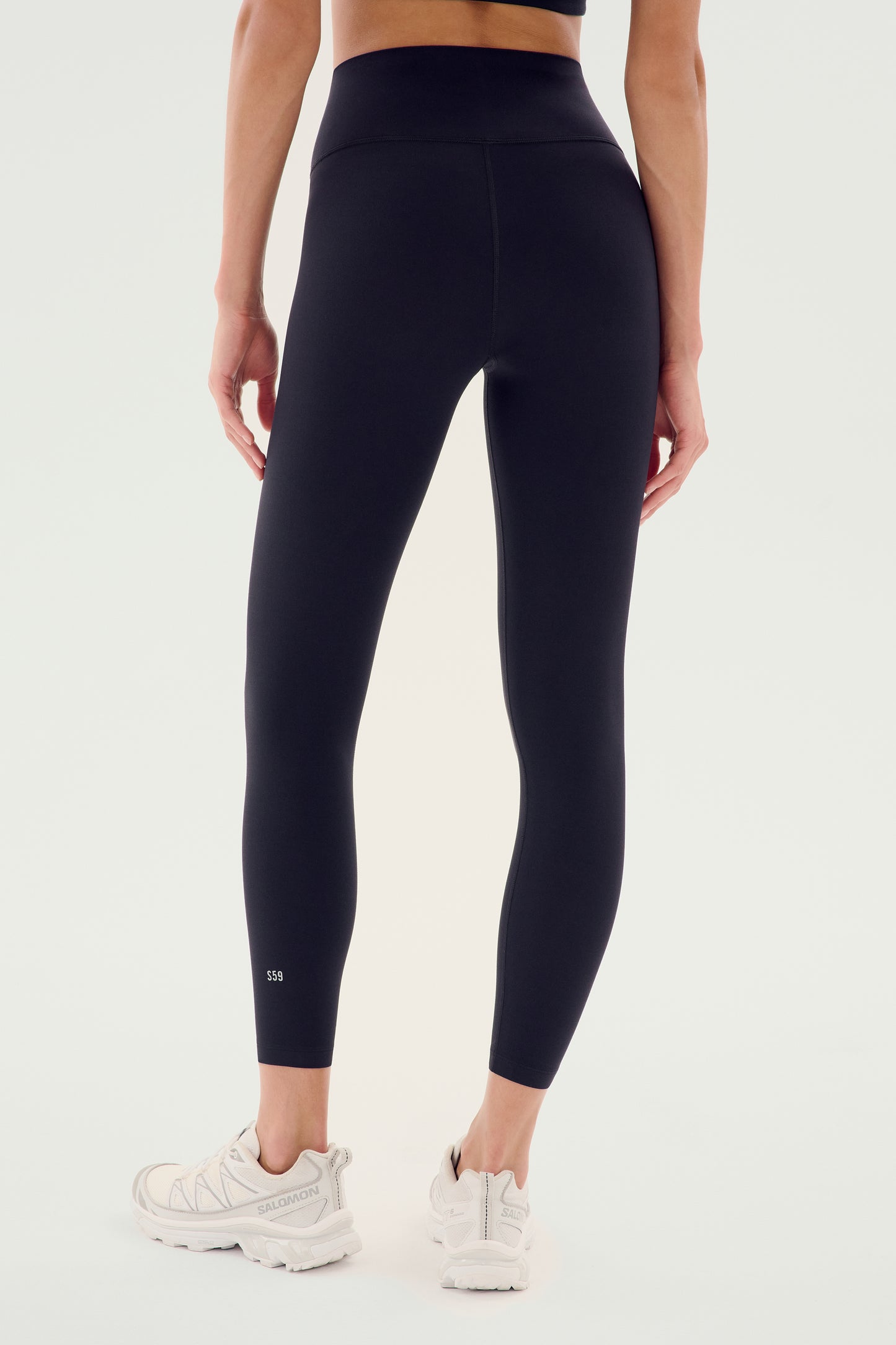 A person is shown from the back wearing SPLITS59's Airweight High Waist Legging in Black and white athletic shoes, making it an ideal outfit for hot yoga sessions.