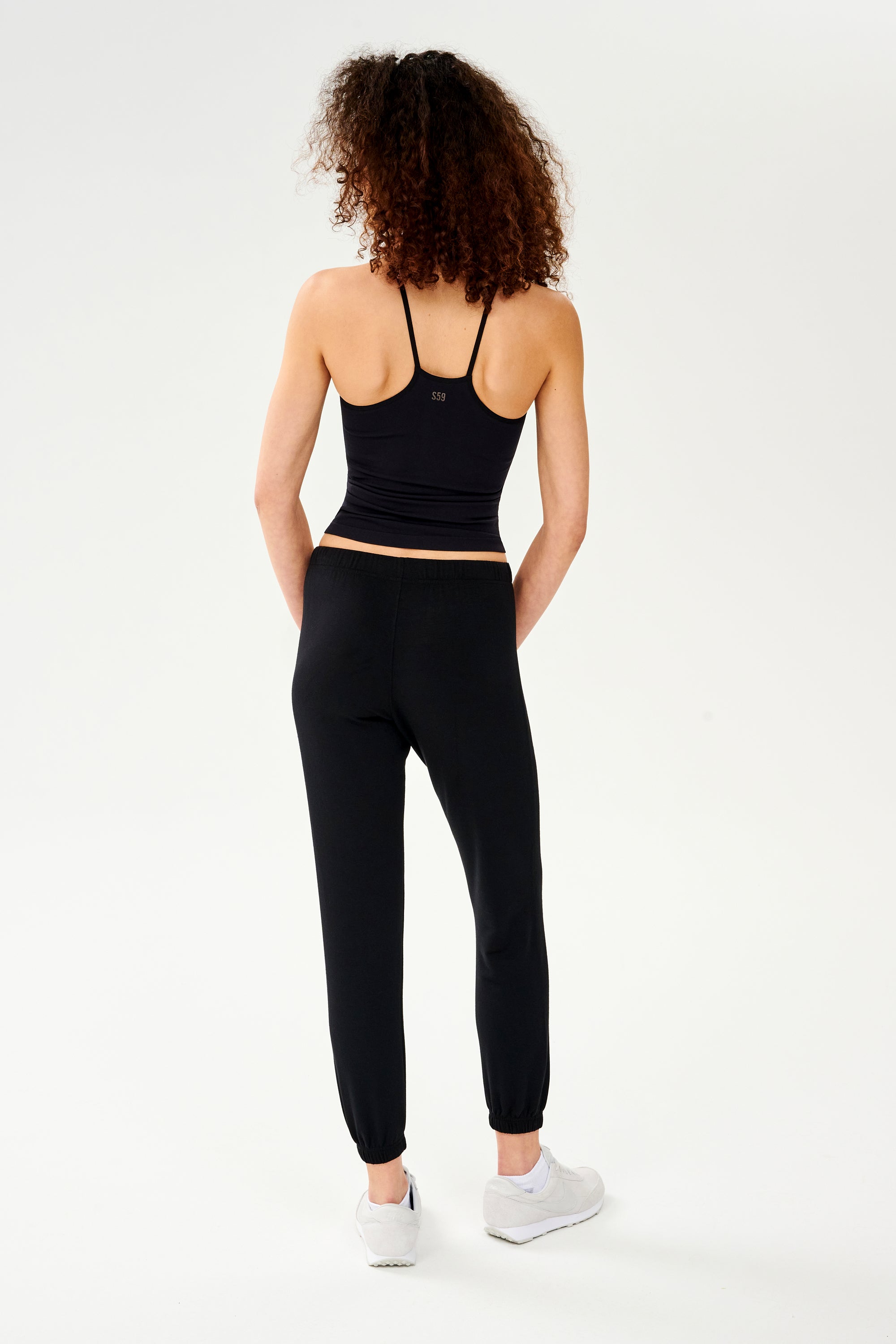 The back view of a woman wearing black joggers and a SPLITS59 Loren Seamless Waist Length Tank - Black.