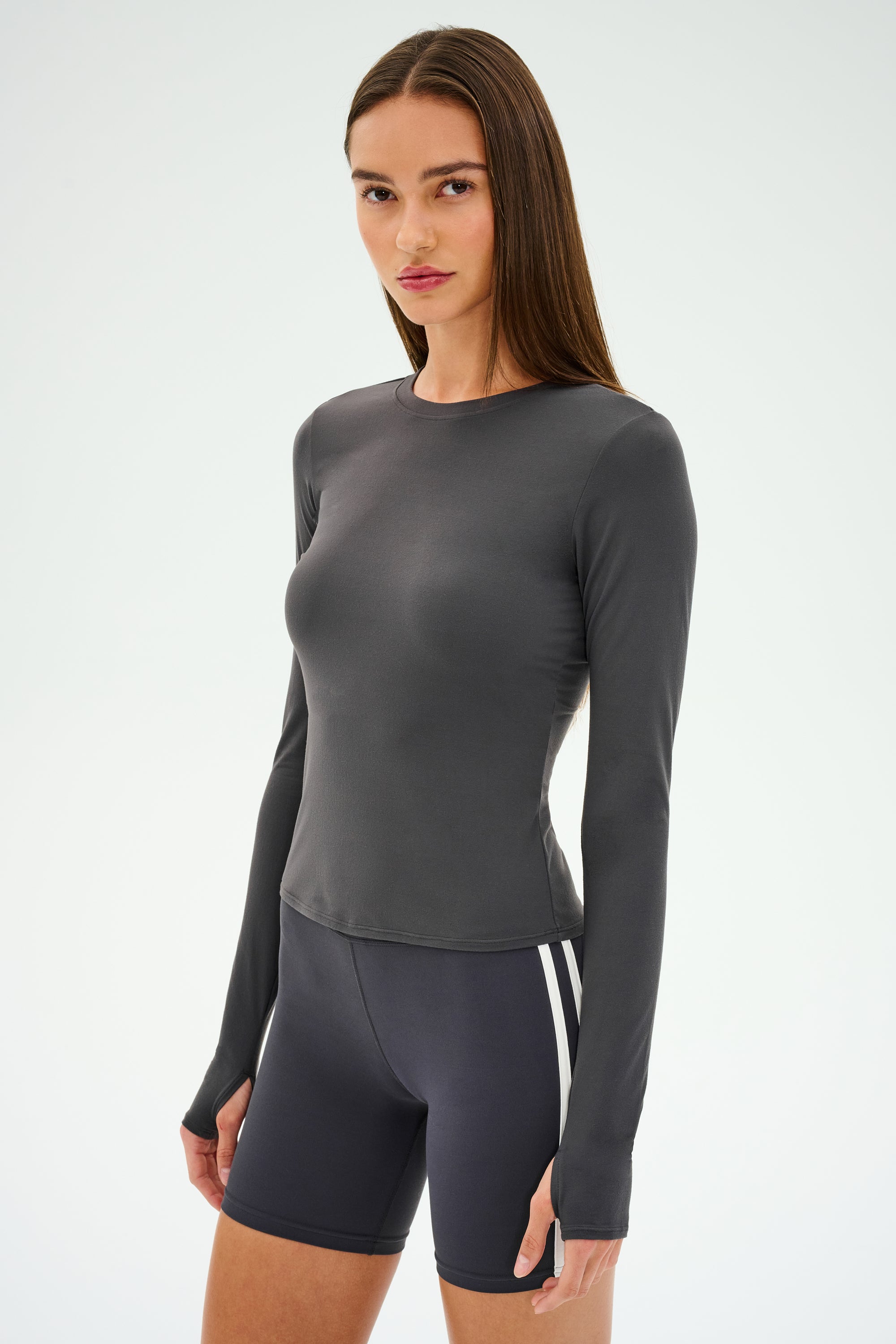 A person wearing the SPLITS59 Airweight Lite LS Waist Length in Graphite and black shorts with white stripes, designed for quick-dry comfort during gym workouts, stands against a plain background.