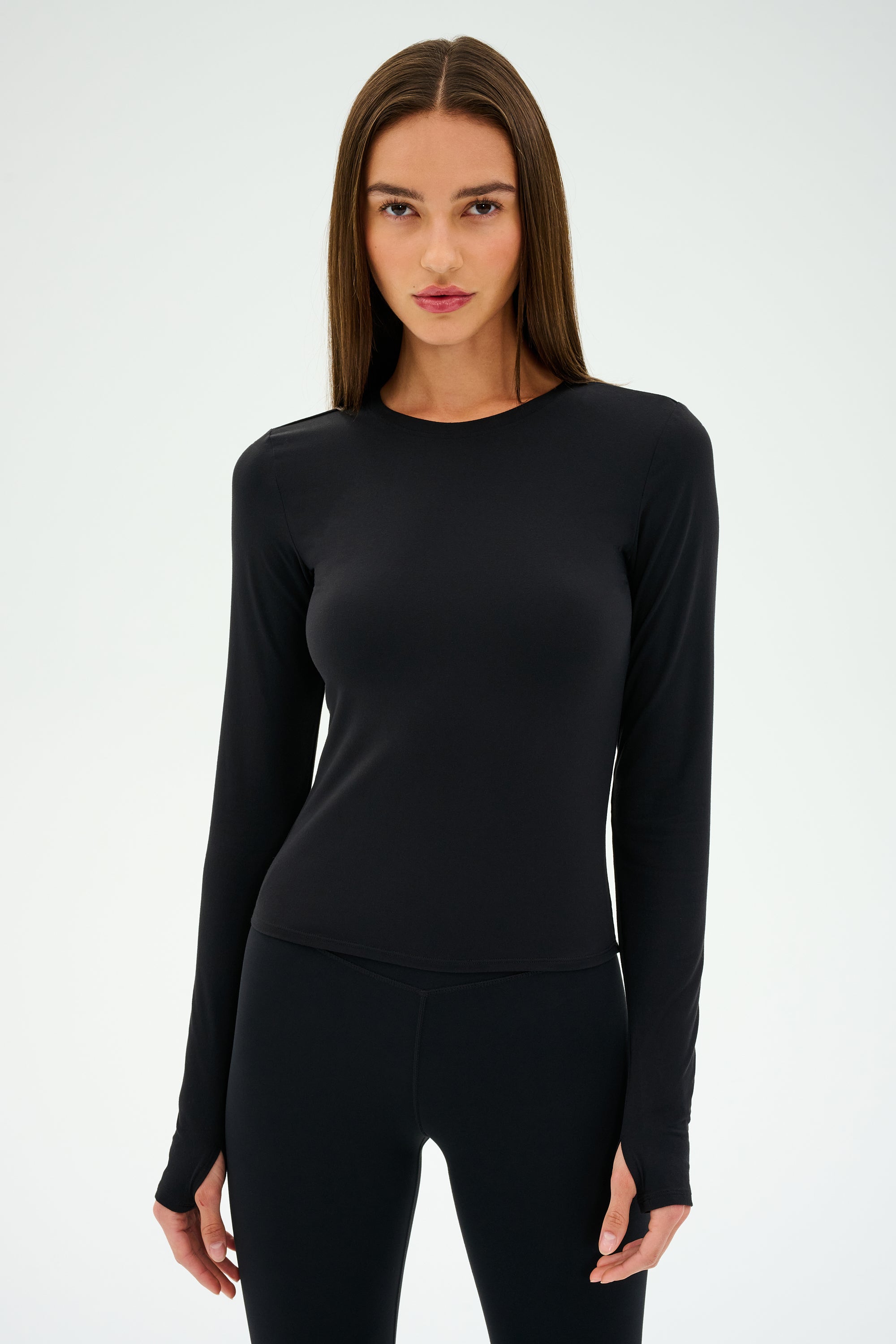 A person with long brown hair wearing the SPLITS59 Airweight Lite LS Waist Length top in black stands against a plain background.